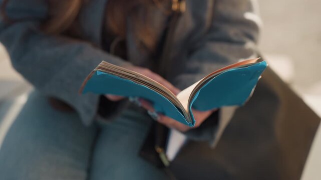 Pretty turquoise journal on lap caucasian woman commuter flips pages while waiting outdoors denim and gray coat visible, candid bench scene in city, tactile paper and stitched cover, travel notes