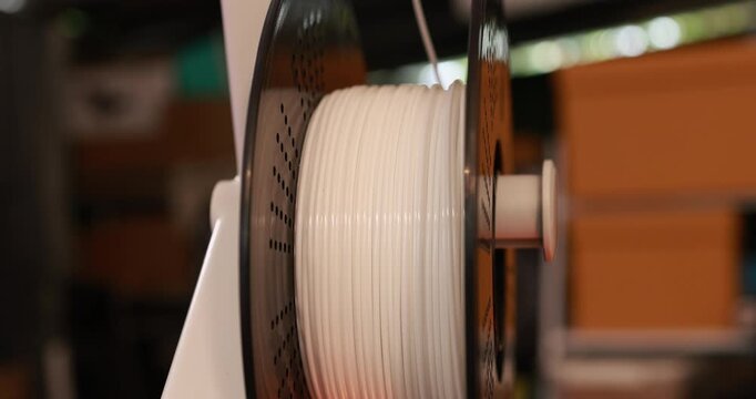 Close-up of white 3d printer filament spool on a reel in a workshop, equipment for additive manufacturing and creative printing