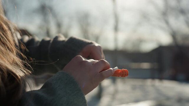 Pretty woman hands opening orange pill bottle outdoors in cold sunlight. Closeup of fingers unscrewing cap and pouring capsules into palm, winter neighborhood backdrop with bare trees, candid intimate