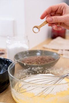Pastry recipe. Dessert preparation. Baker female adding measured salt sugar spoon portion to bowl with sweet dough on kitchen countertop.