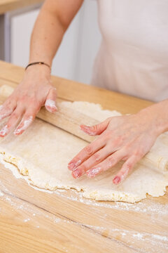 Bakery workflow. Pastry recipe. Female confectioner hand rolling dough sheet with kitchen pin on flour home countertop making dessert.