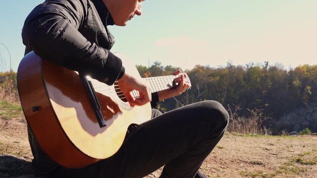 Close up hands of artist plays wooden acoustic guitar in autumnal park. Young songwriter plays string musical instrument hobby outside in nature fall time. Audio music healing in natural surrounding. 