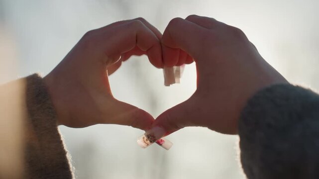 Hands forming pretty heart shape sunlit soft backlight winter coat sleeves delicate manicure warm glow through heart slow motion intimate romantic mood dreamy bokeh natural outdoor morning