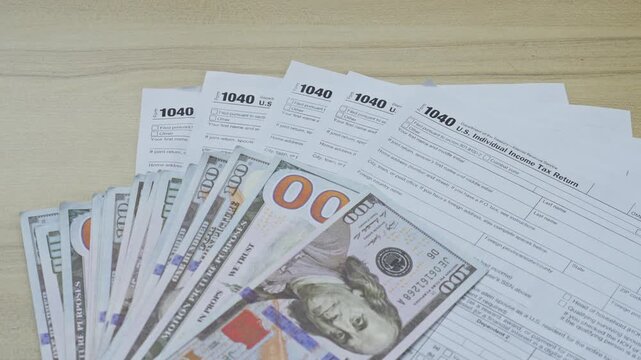 Hand places fan of hundred-dollar bills on top of blank U.S. Individual Income Tax Return 1040 forms