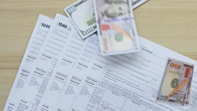 Hundred-dollar bills are dropped or thrown onto U.S. individual income tax return 1040 forms