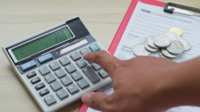 Hand counts coins and uses a calculator next to U.S. individual income tax return 1040 form