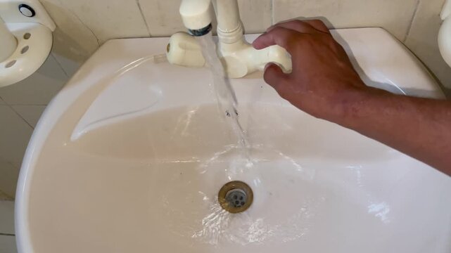 Hand opening a bathroom faucet tap with running water