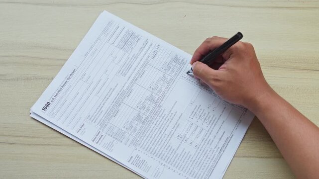 Hand fills out U.S. individual income tax return 1040 form using pen