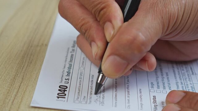 Hand uses pen to write on U.S. individual income tax return 1040 form
