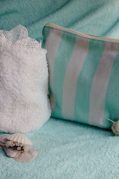A fluffy white towel provides a serene background, a toiletry bag, delicate seashells, and a piece of crocheted lace evoke themes of relaxation and well-being.