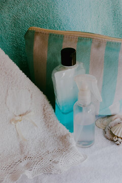 Refreshing spa set on white towels featuring blue and clear skincare products, a striped cosmetic bag, and seashells, symbolizing self care, beauty, and relaxation