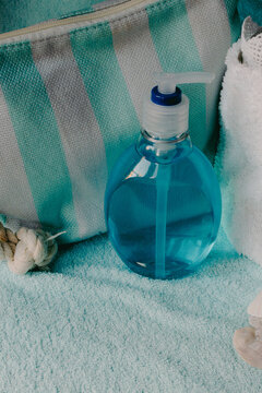 Blue liquid soap bottle for hygiene and relaxation, standing on a soft towel next to a striped toiletry bag, symbolizing self-care and peaceful spa routines