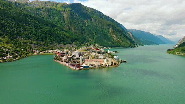 Aerial drone footage of Boliden Odda, a major zinc smelter located on the shore of S&oslash;rfjorden near Odda, Norway. The industrial complex stands against a dramatic landscape of steep green mountains 