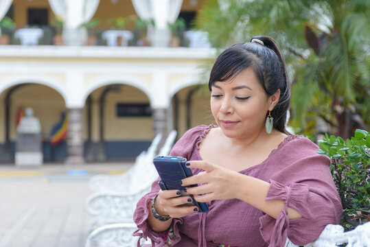 Latina Woman Typing on Smartphone While Sitting on White Bench Outdoors