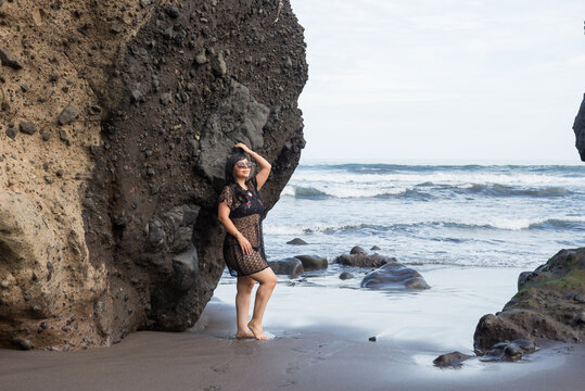 Smiling Woman in Black Lace Outfit Standing in Ocean Waves by Volcanic Cliff