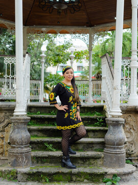 Confident Woman in Floral Embroidered Dress Posing in Ornate White Gazebo