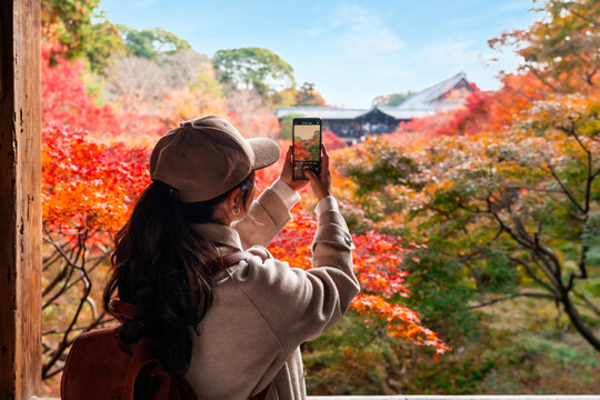 Solo female tourist taking a photo of beautiful scenic view and vibrant autumn foliage at Tofuku-ji temple in Kyoto