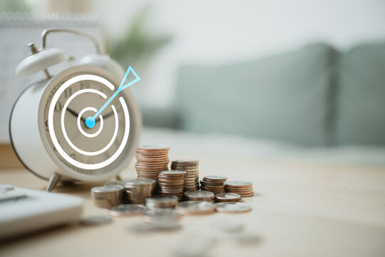 Tracking savings goals with coins, an alarm clock, and target icon symbolizes financial planning, budgeting, and steady progress toward future security.