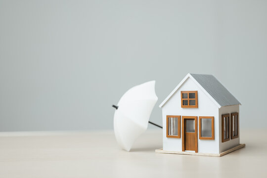 Home with an umbrella represents insurance coverage, property protection, and financial security against unexpected risks and disasters.