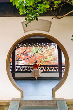 Young female tourist relaxing and enjoying the view of red maple leaves during the autumn foliage season at Hangzhou, China