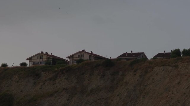 Houses perched on a coastal cliff in Sopelana, Basque Country, offering views of the Cantabrian Sea under a grey sky