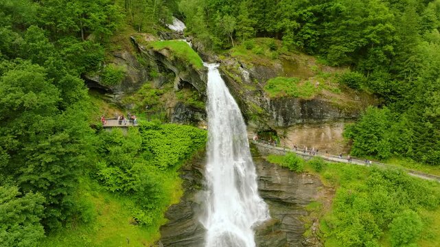 Aerial view of Steinsdalsfossen waterfall in Norway, surrounded by lush green forest and rocky cliffs. The drone flies smoothly forward while gradually tilting the camera, revealing the full height 
