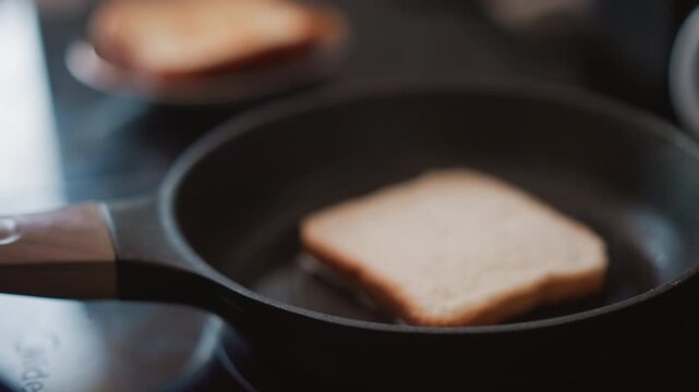 Pouring oil into pan white woman adds thin stream of oil over bread slice, controlled motion, warmed skillet on induction stovetop, quiet kitchen routine, concentrated hands and precise cooking step