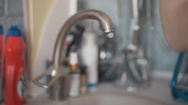 Mint board held near dripping faucet, closeup of chrome spout and water droplets, blurred cleaning bottles on countertop, soft bokeh and ambient morning light, casual hand hovering in after cleaning