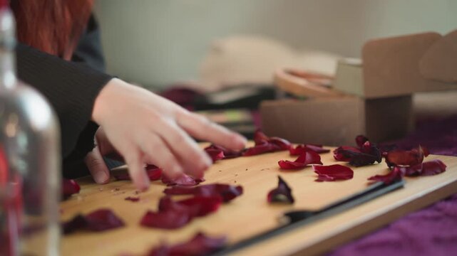 Hands arranging red petals on wooden board, preparing petal divination spread with careful fingertips, scattered rose fragments, soft bokeh, deliberate movements and focused tactile ritual