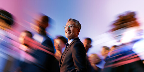 Obraz premium Smiling Asian Executive With Glasses Looking Forward Through Blue Pink Business Crowd Blur