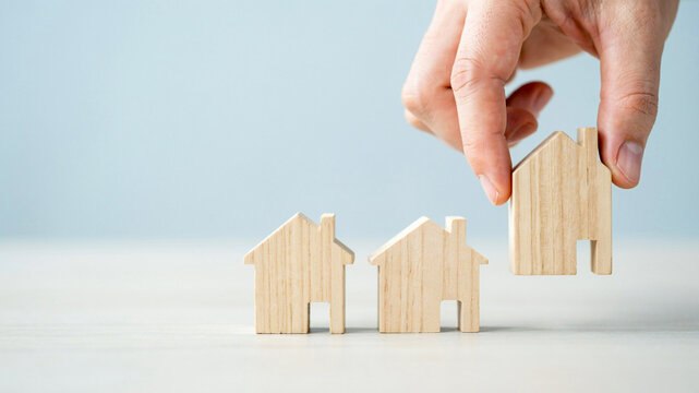 Hand choosing miniature wooden house model real estate property concept
