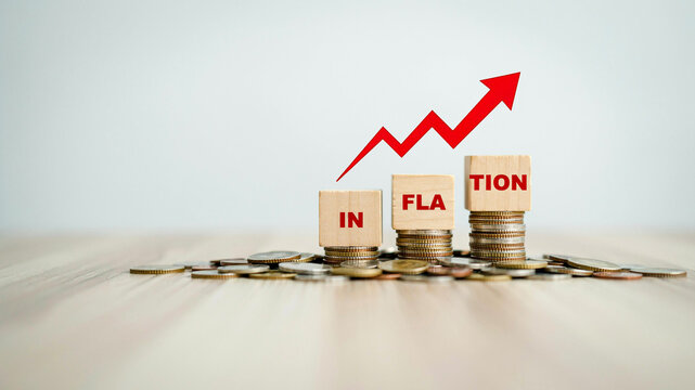 Concept of inflation represented by wooden blocks spelling the word on piles of coins with a red growth arrow pointing up