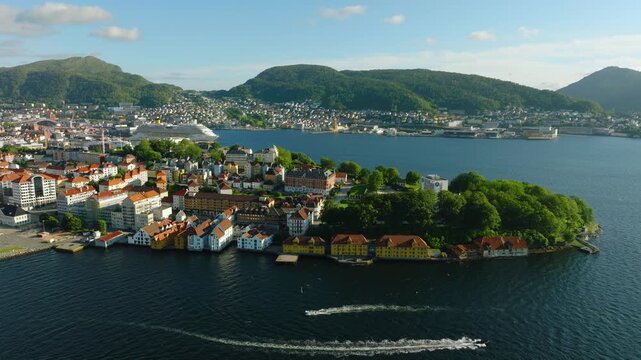 Smooth drone orbit around Nordnes Peninsula in Bergen, Norway, revealing the waterfront, colorful historic buildings, surrounding harbor waters and green mountains of the city.