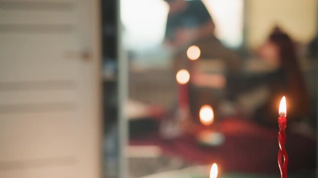 Observer watches carefully. Redhead watches dim room ritual. Woman with red hair observes candle ritual attentively. Brunette closely watches flickering ceremony within dimly lit space