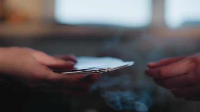 Hands exchanging tarot cards amid smoke, apprentice reader passes deck over velvet cloth, smoke curling from extinguished candle, closeup fingertips and nails, ritual rhythm, tense cinematic mood,
