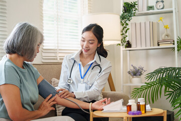 Fototapeta premium Asian nurse checking senior woman blood pressure at home for senior healthcare checkup
