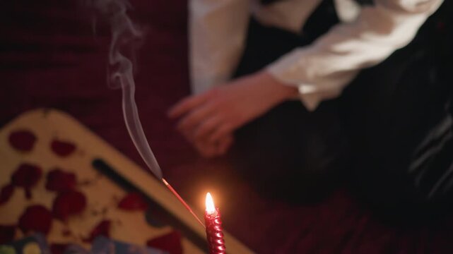 White woman fortune teller reading tarot in dim velvet room, candle flame casting glow, incense smoke drifting, scattered rose petals, hand hovering over cards, intimate ritual, vintage aesthetic,