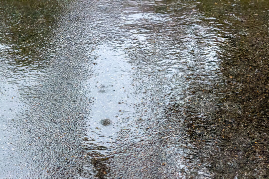 rainwater puddle background with sky reflection and raindrops rippling.