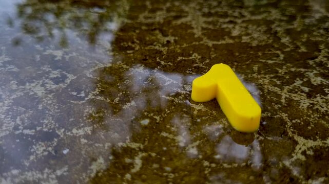 Bright yellow number one symbol lying in shallow puddle on cracked concrete water wet digit