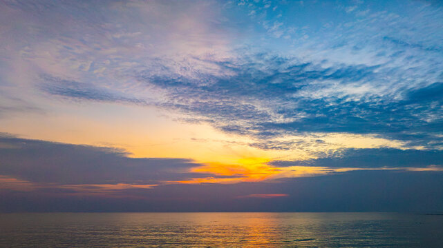 A nature sky panoramic scenic view of a vibrant sunset or sunrise sky with glowing orange and yellow clouds transitioning into deep blue twilight, representing nature beauty, and tranquility at ocean
