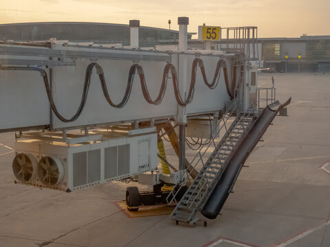 Calgary, Alberta, Canada. August 9, 2026. Side view of airport jet bridge gate 55 and baggage chute on tarmac at terminal during sunset.
