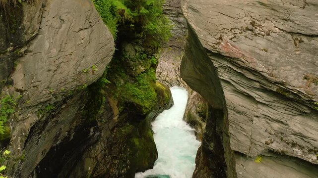 Cinematic drone footage of the Valld&oslash;la River rushing through the narrow rocky gorge at Gudbrandsjuvet in Valldal, Norway. The drone slowly pulls back and rises, gradually revealing the historic stone