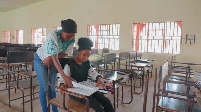 Black mother tutoring child in classroom, sunlit empty room with rows of desks and curtains, mother leaning over student pointing at workbook, gentle supportive guidance, focused child reading