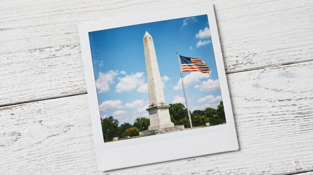 Polaroid photo of Washington Monument and American flag on white wood.