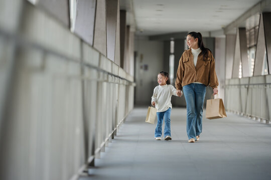 happy mother and child girl with shopping bag walking on footbridge in city