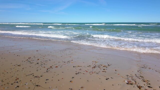 Empty sandy beach of Grenen, Denmark, with gentle waves and blue sky on a calm summer day. Walking, motion.