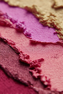 Makeup powder showing vibrant crushed texture. Shades of pink, purple, and gold creating an abstract, artistic background