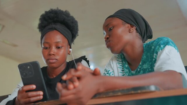 Black mother and daughter using smartphone together, desk view, mother demonstrating app, daughter scrolling, shared discovery, digital lesson, social media glance, steady hands, attentive expressions