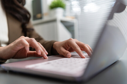 Close-up of a businesswoman typing on a laptop keyboard in a modern workspace, representing online business, remote work, digital technology, communication, and productivity.