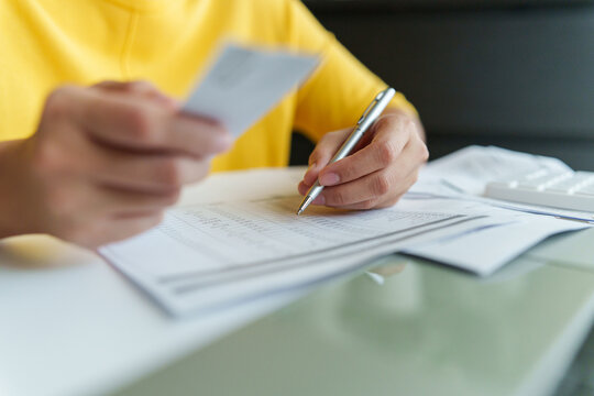 Woman reviewing household bills and financial paperwork while holding a payment card, managing monthly expenses, budget, debt, utilities, and personal finances at home.